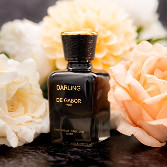 un flacon de parfum noir devant des roses blanches