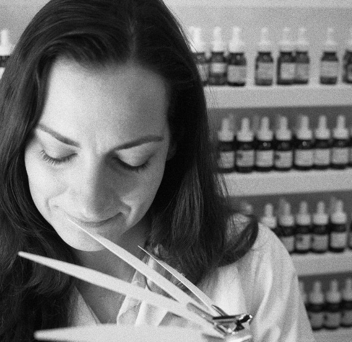 Photo en noir et blanc de la parfumeure Camille Leguay, prise dans son laboratoire, pour promouvoir sa propre marque de parfums de niche. Elle tient des mouillettes dans la main.