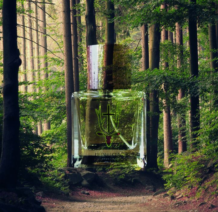 Un flacon de parfum de niche LE DIEU CERF de grande taille, placé dans une forêt verdoyante. On  voit la nature au travers du flacon