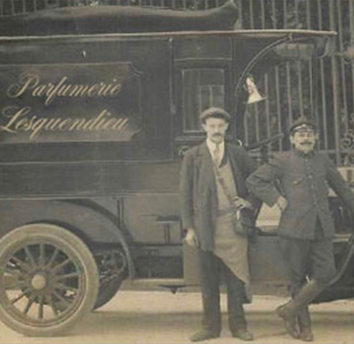 Une photo ancienne en noir et blanc montrant une camionette LESQUENDIEU, avec un homme en tenue de chauffeur et un autre en tenue d'ouvrier