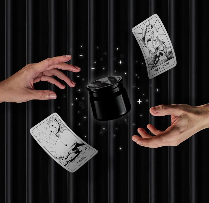 Hands reach for a pot of black beauty cream floating in the air, surrounded by twinkling stars. Two black and white tarot cards flutter around the hands.