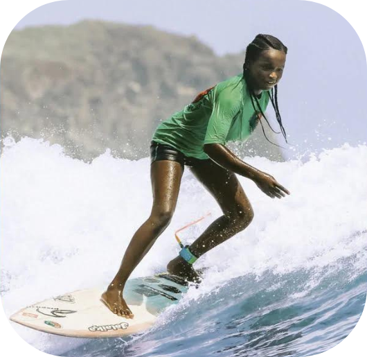 An African woman wearing a t-shirt from south-african brand MAMI WATA is surfing.