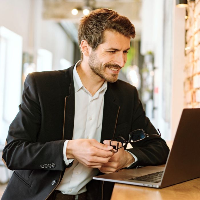 Un homme dans la quarantaire est dans son appartement. Il porte une veste en velours sombre. Il regarde l'écran de son PC portable en souriant. Il consulte les avantages du programme de fidélité de SCENTISSIME