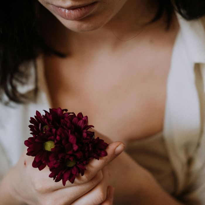 Une femme brune habillée en blanc tient dans ses mains quelques fleurs rouges.